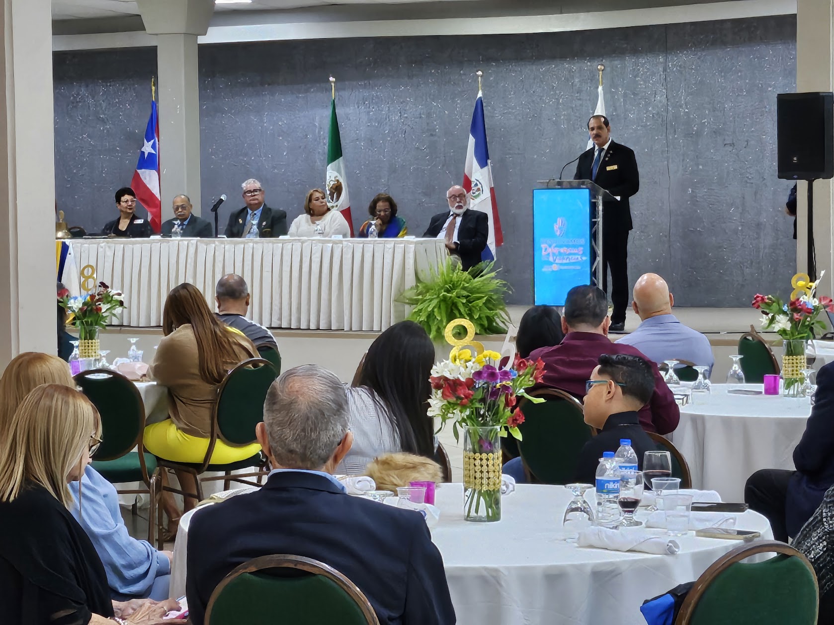 Salón de una Conferencia de Distrito con socios reunidos, banderas y ambiente de compañerismo.