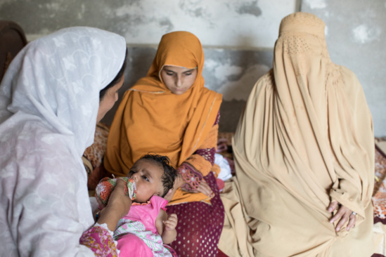 Una trabajadora de la salud, habla con una mujer y vacuna a su hijo durante una campaña puerta a puerta en Nowshera (Pakistán).
